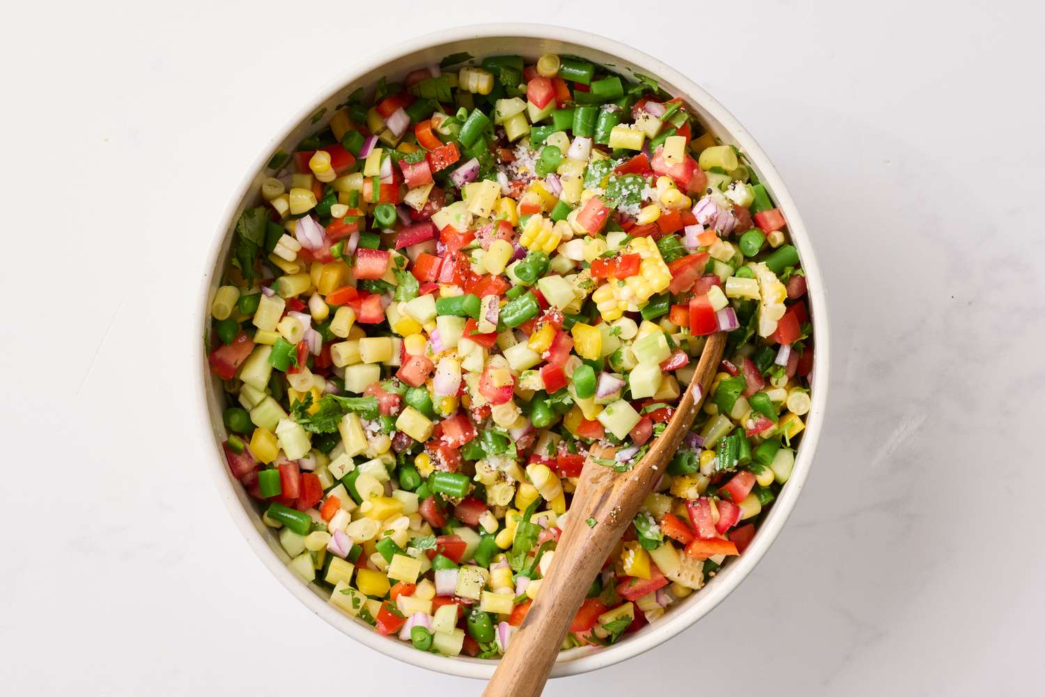 A bowl of chopped vegetable salad with a wooden spoon