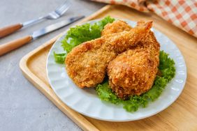 Three pieces of fried chicken on a bed of lettuce served on a white plate with cutlery nearby