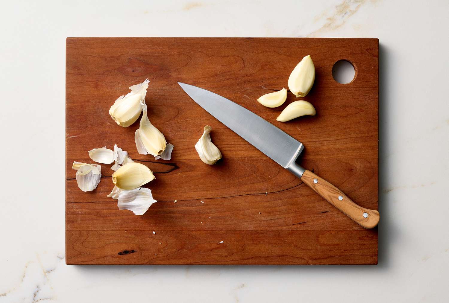 Garlic cloves and a knife on a wooden cutting board