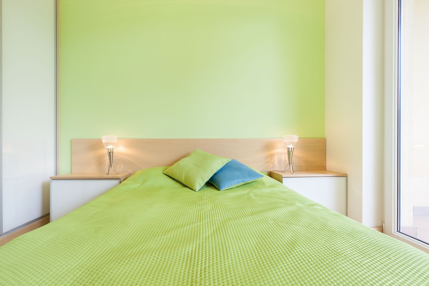 A neatly made bed in a bedroom minimalistic decor with two pillows and bedside lamps limegreen wall in the background