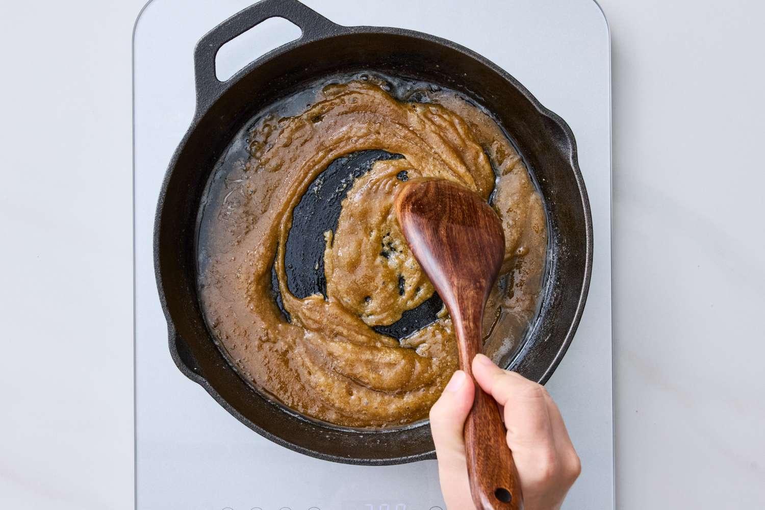 A hand stirring caramellike mixture in a castiron skillet on a stovetop