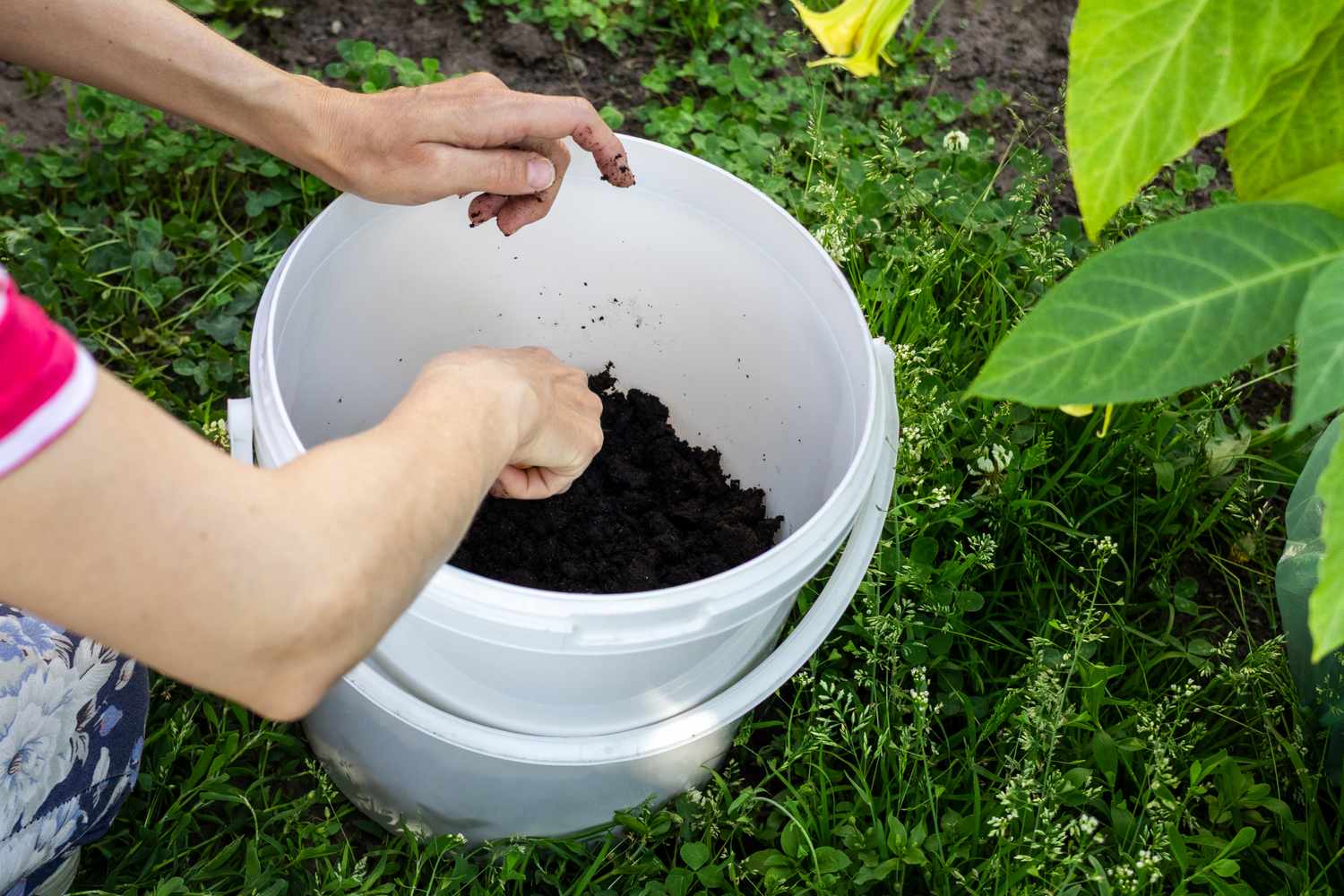 Person mixing soil in a white bucket preparing for gardening or planting
