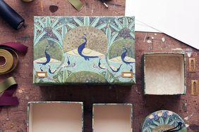 Decorative boxes with peacock designs on a wooden surface surrounded by crafting materials