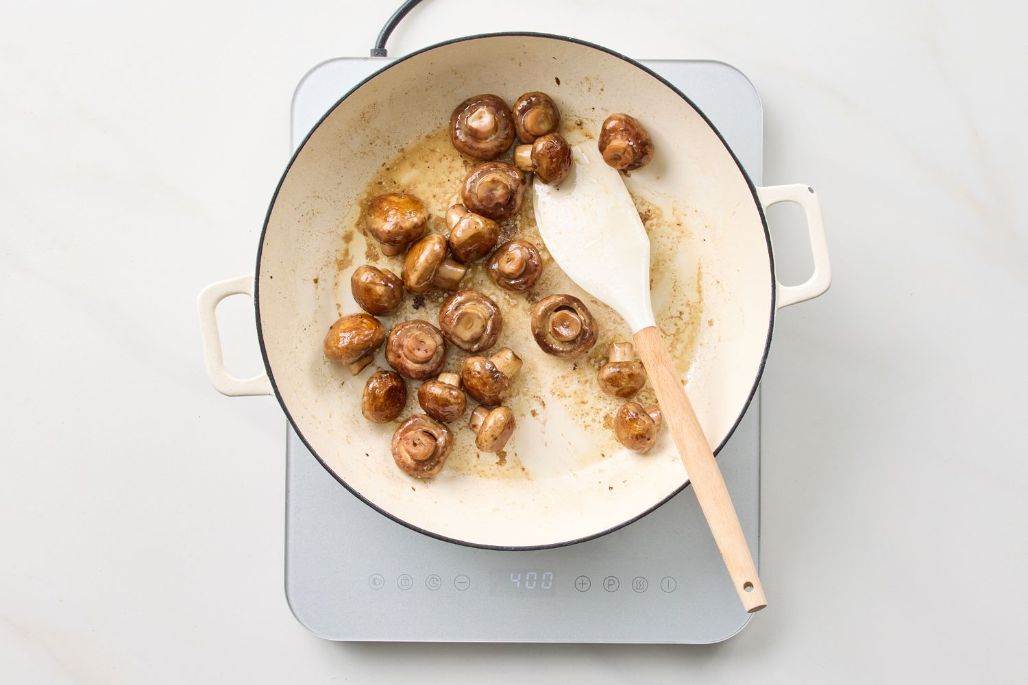 Sauted mushrooms in a pan with a spatula placed on a stove
