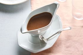 A white sauceboat filled with brown sauce placed on a white plate with a spoon beside it