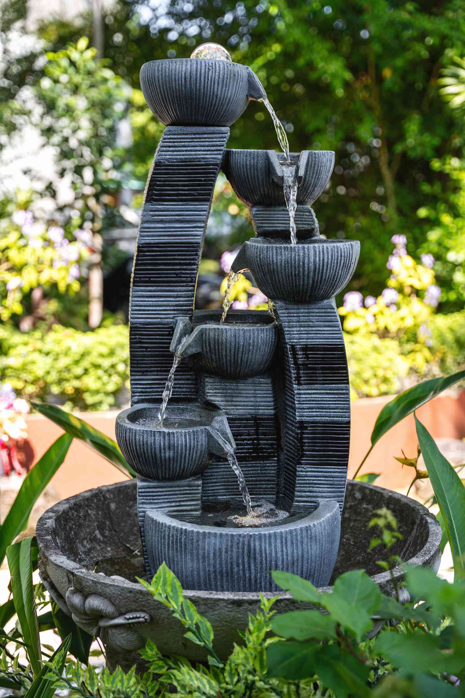 A water fountain with concentric bowls trickles water in a picturesque garden.