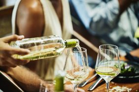 A person pouring white wine into a wine glass at a dining table