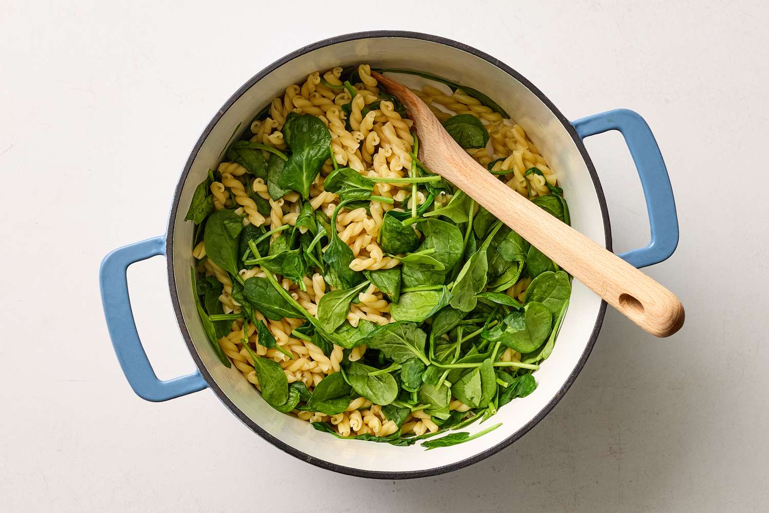 Pasta with fresh spinach in a pot with a wooden spoon