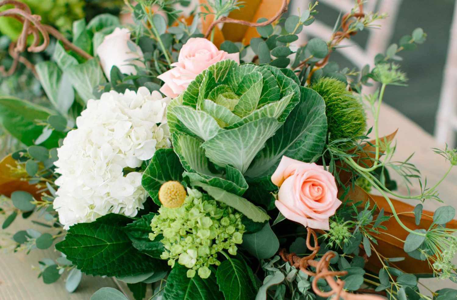 A floral arrangement featuring leafy greens roses and white hydrangeas on a table