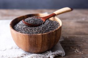 A bowl filled with chia seeds with a wooden spoon on a wooden surface