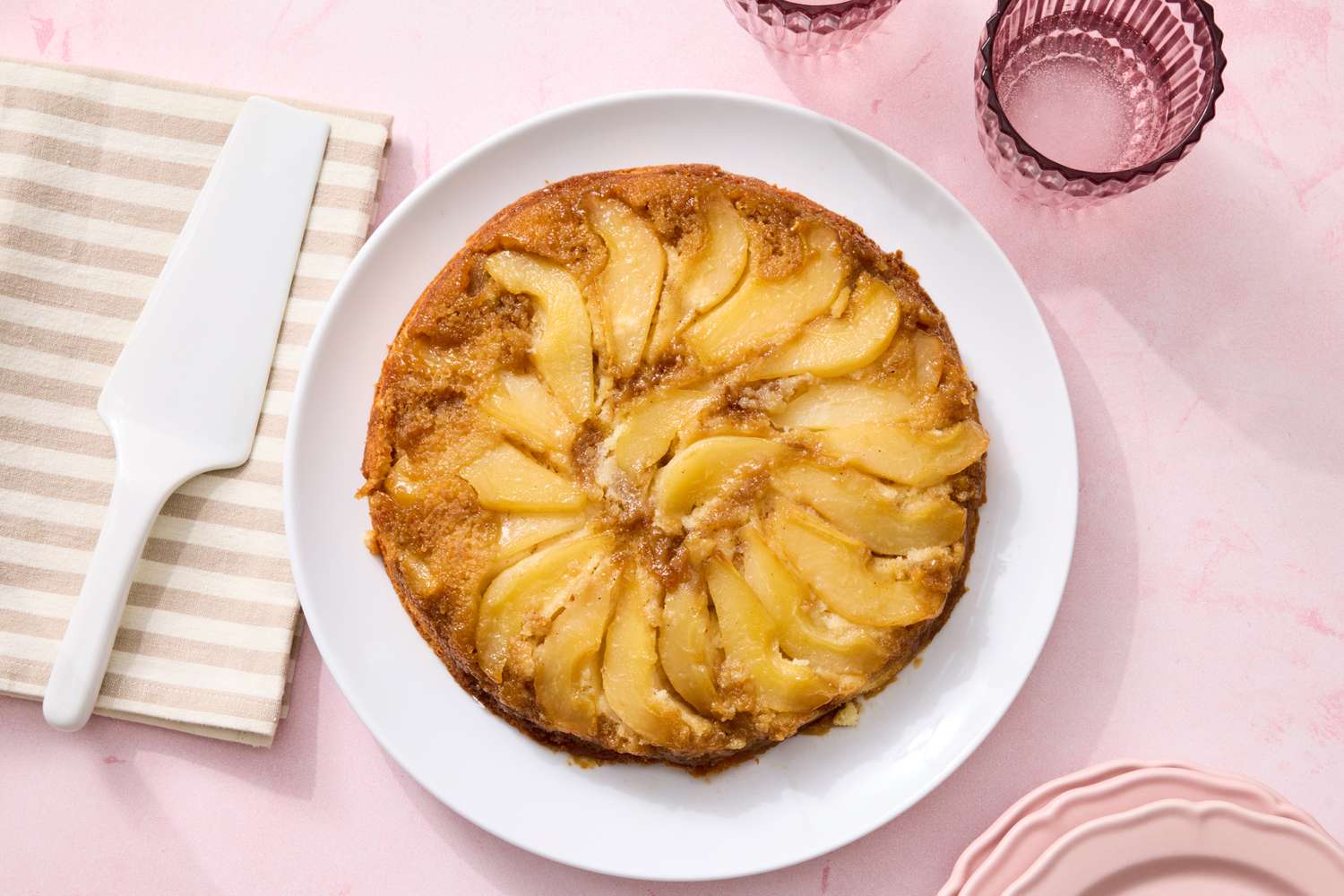 Pear upsidedown cake on a white plate surrounded by glassware and a napkin