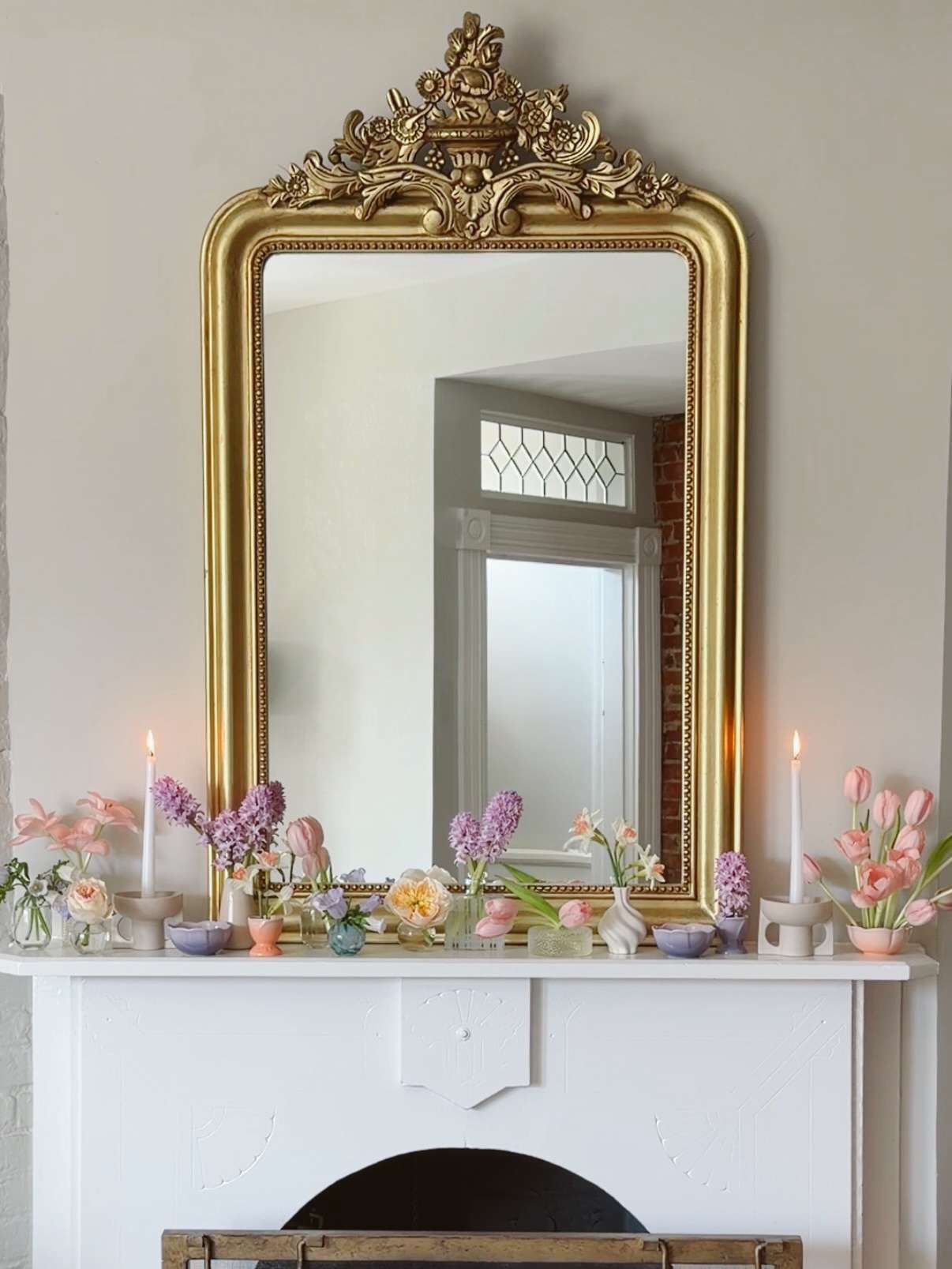 A goldframed mirror above a mantel decorated with pastel flowers and candles spring decor style