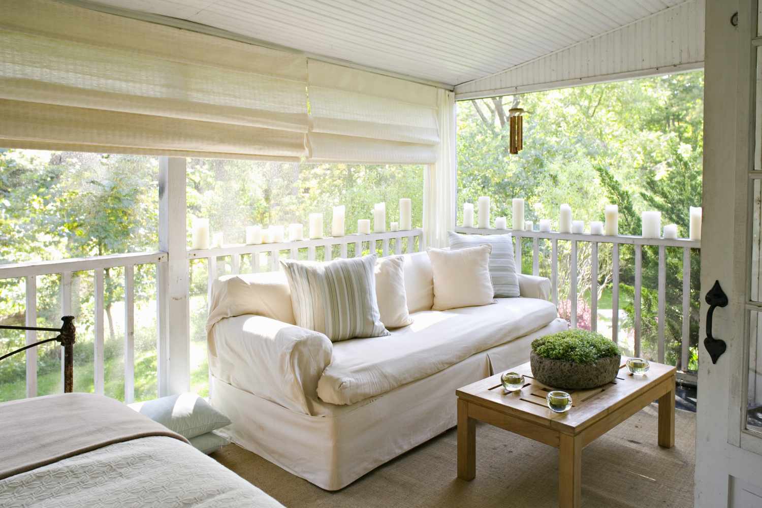 A porch with a couch a coffee table and cushions surrounded by trees