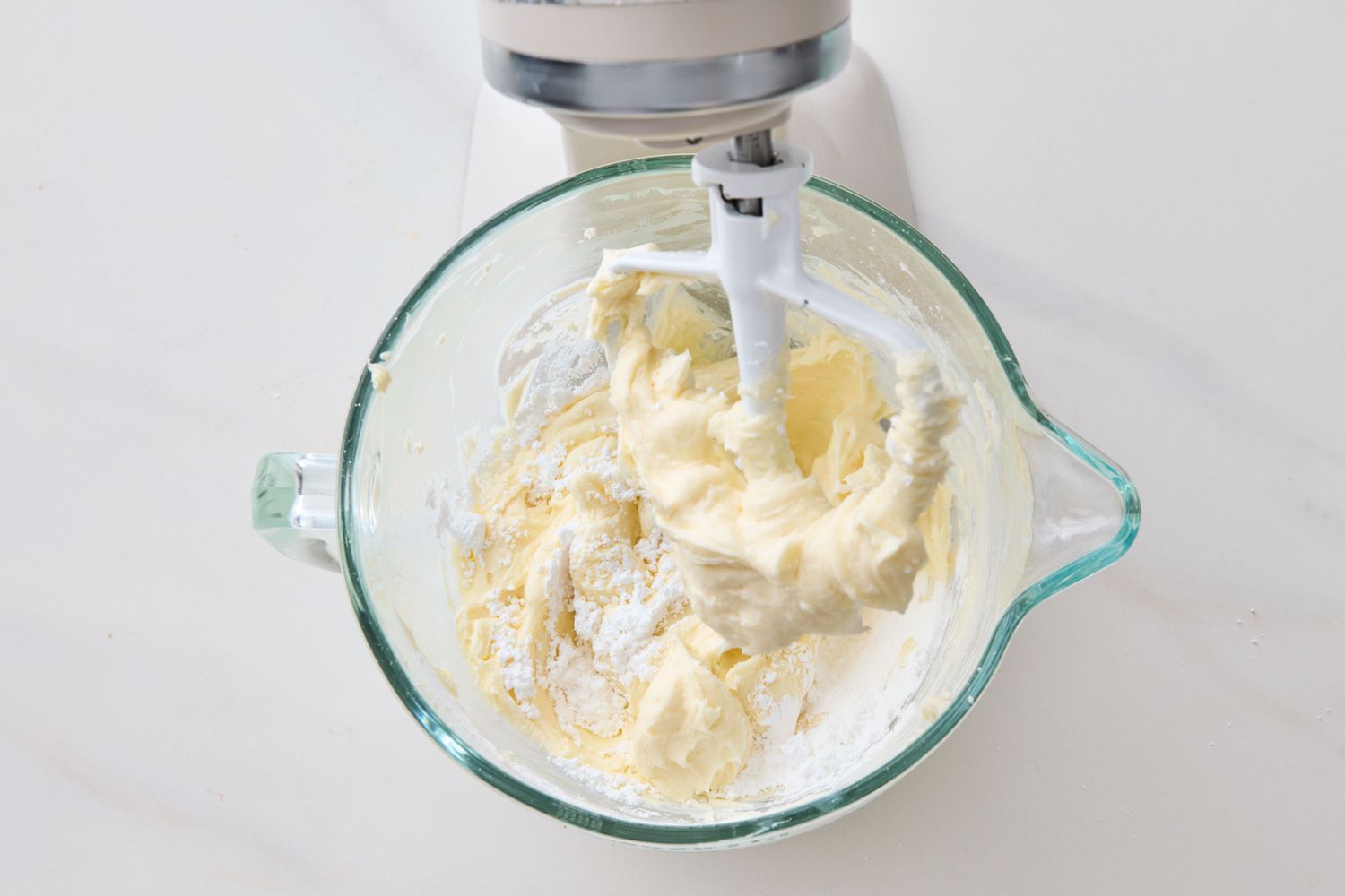 Stand mixer with cream cheese frosting in glass bowl