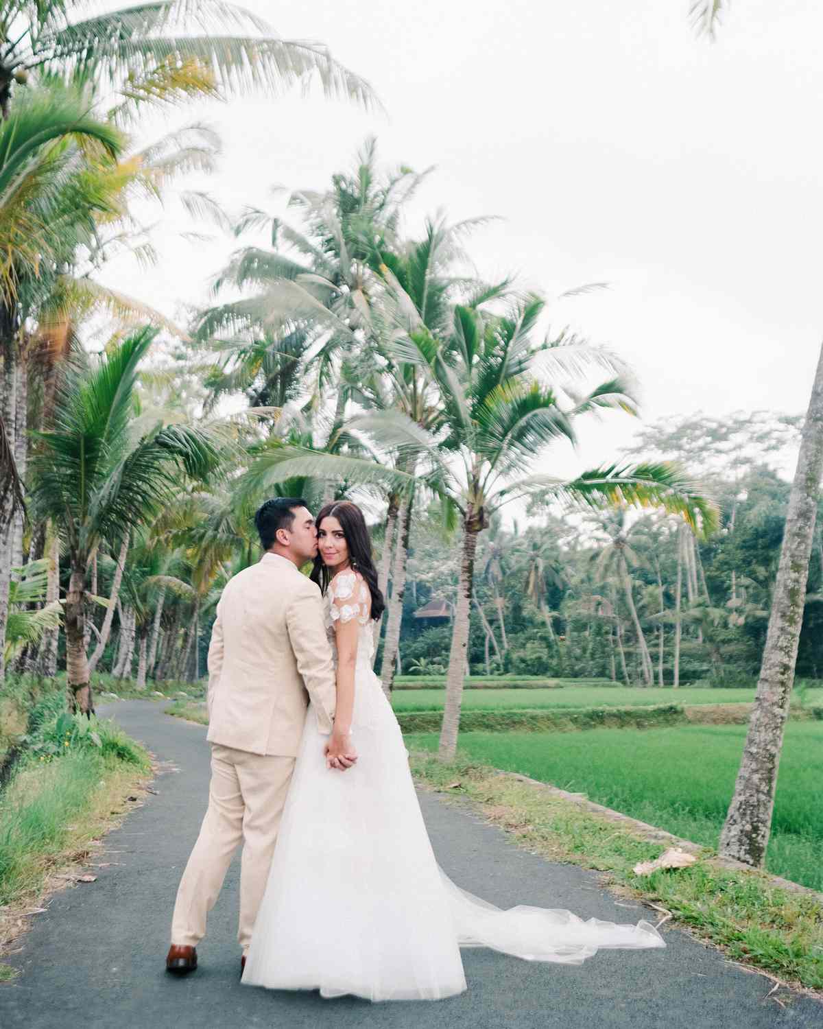 bride and groom holding hands walking along path of palm trees
