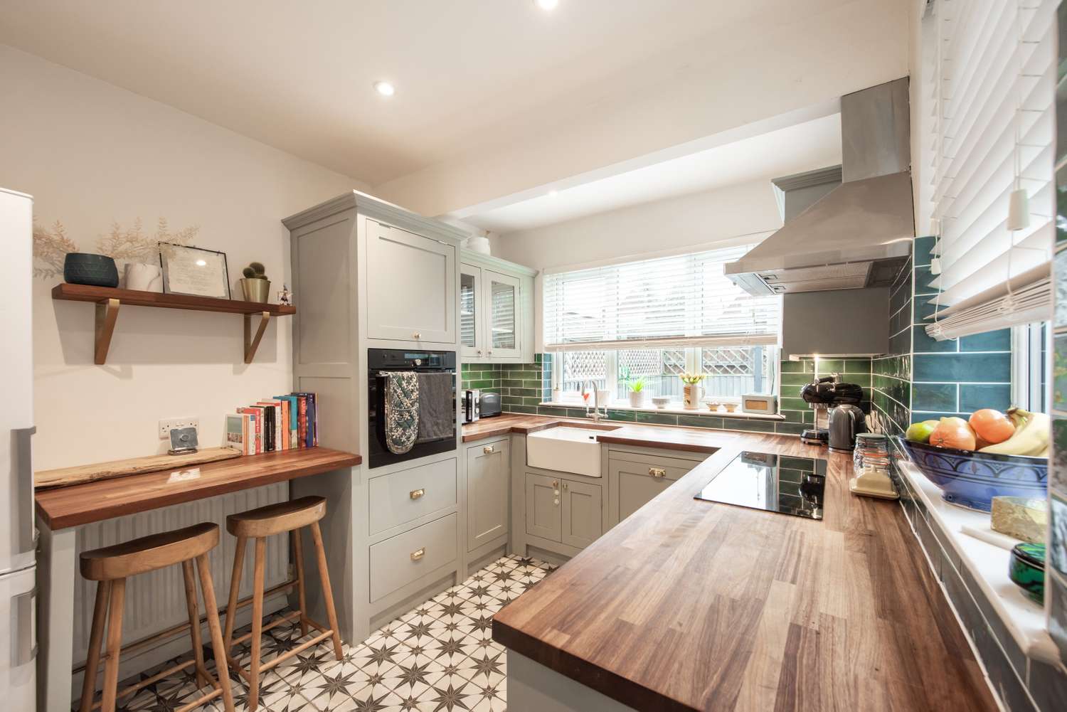 A modern kitchen with a wooden countertop tiled floor and appliances featuring a small dining area with two stools