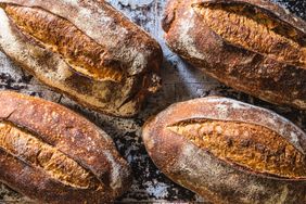 Four loaves of freshly baked sourdough bread with a rustic appearance on a baking surface