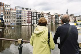 Two people standing by a river with urban wateredge buildings in the background