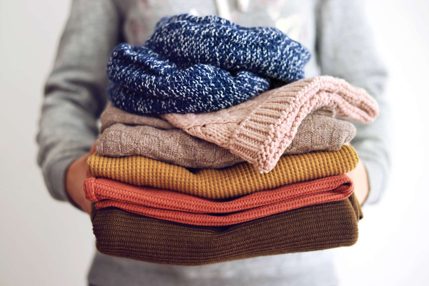 woman holding stack of folded sweaters
