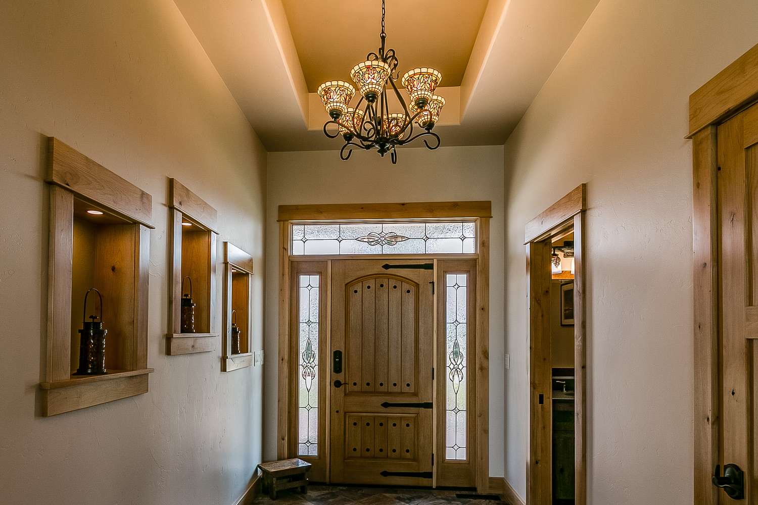 Home entrance with a wooden door and decorative glass panels flanked by inset shelves and a chandelier overhead