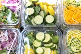 Assorted plastic containers filled with precut vegetables including zucchini slices and spiralized vegetables