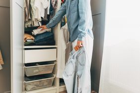 A person organizing clothes in a closet holding a pair of jeans in one hand