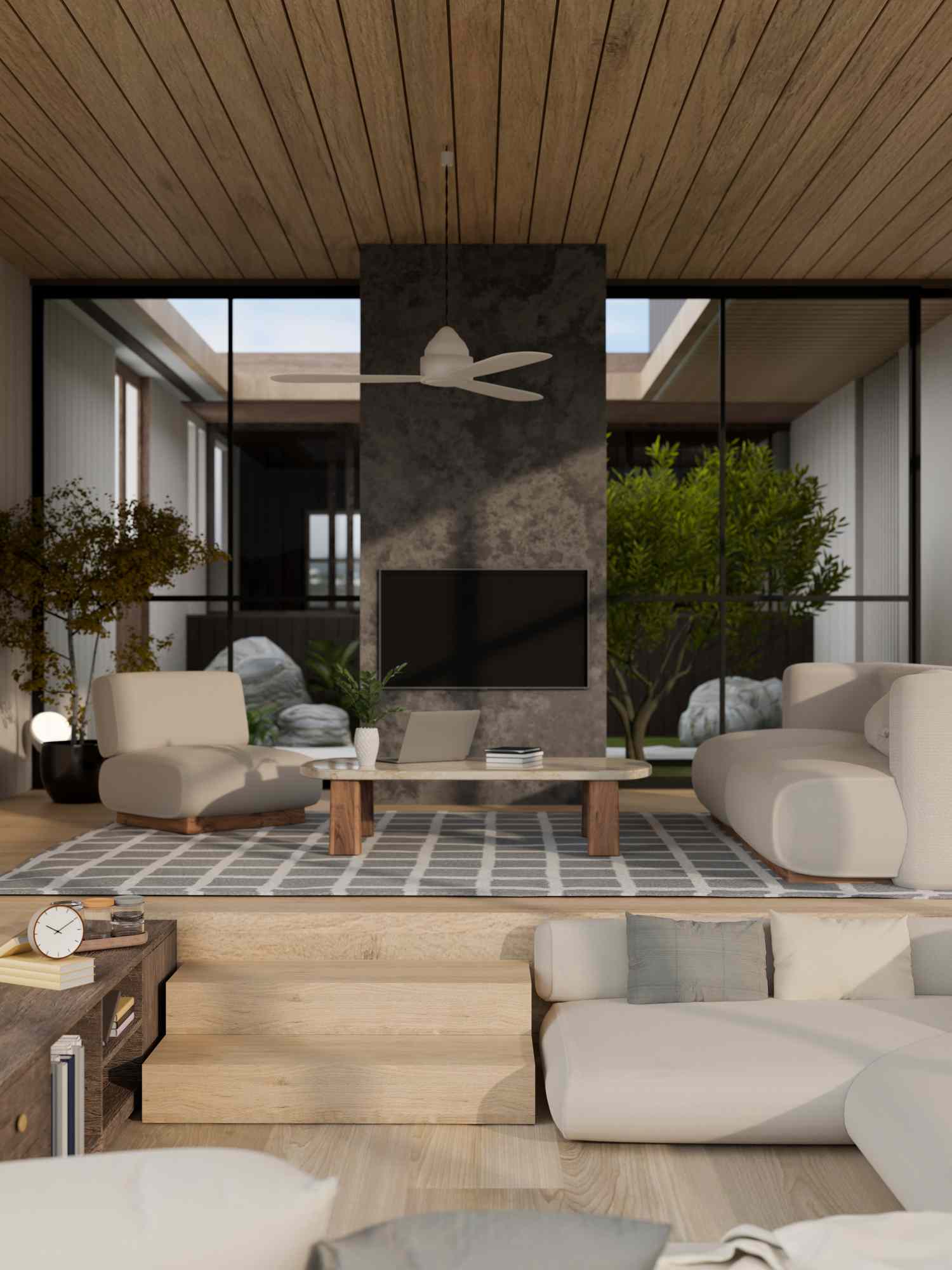 A modern living room with a centered television mounted on a stone wall surrounded by sofas and a view of greenery outside