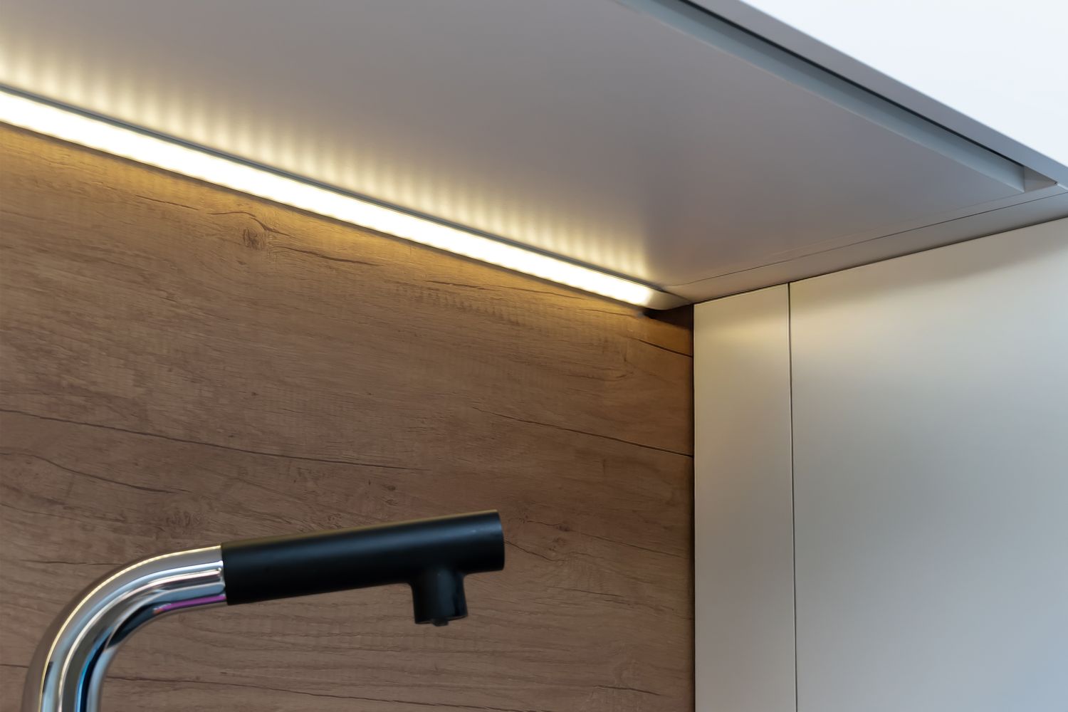 A modern sink faucet under a cabinet with LED strip lighting installed