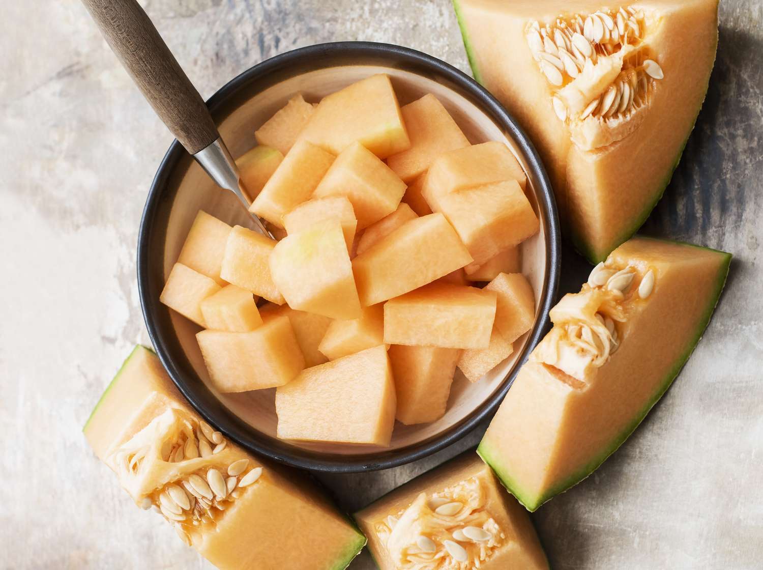 Bowl of cubed cantaloupe with sliced cantaloupe wedges and seeds surrounding