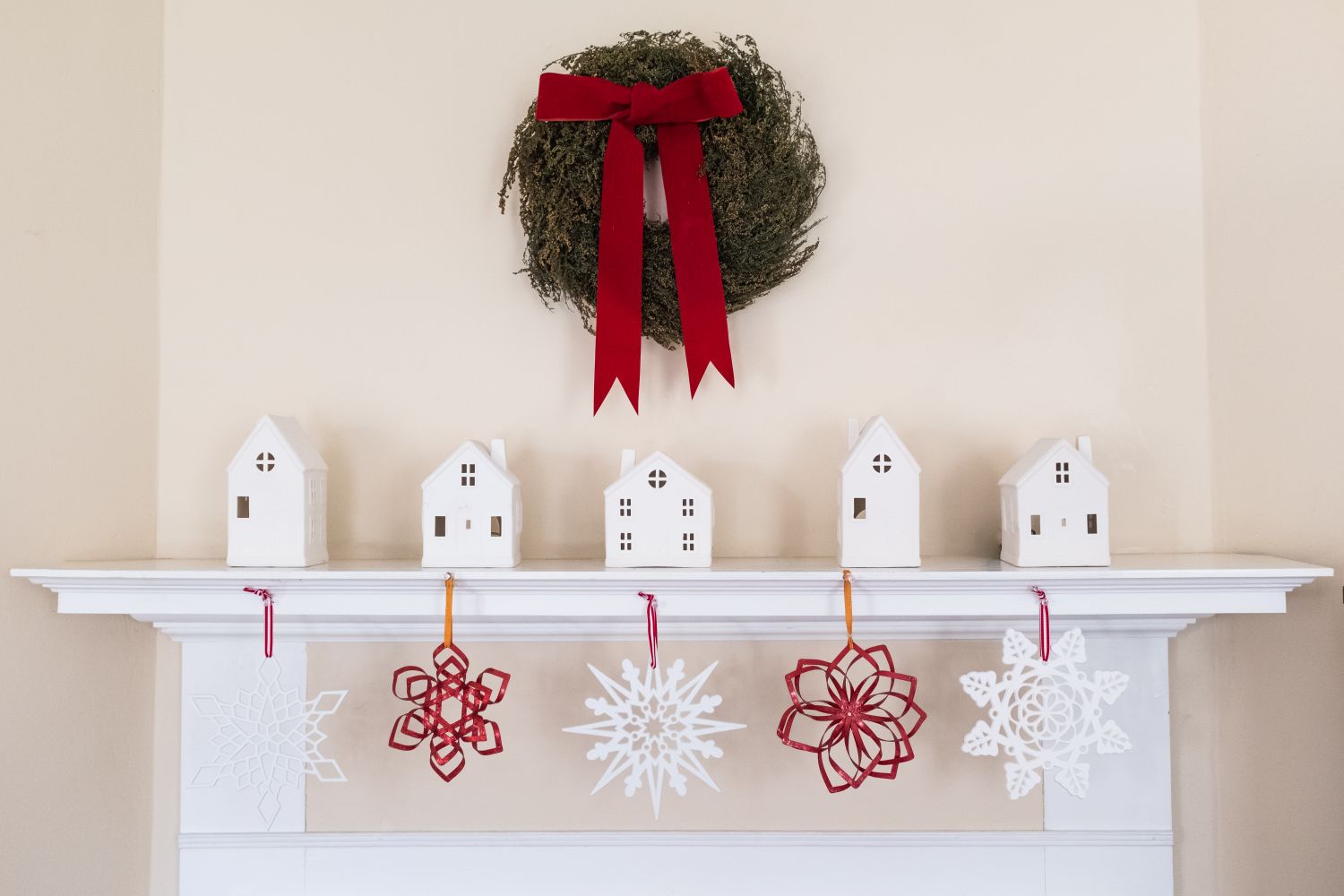 Fireplace mantel with miniature house ornaments decorative snowflakes and a wreath with a red bow hanging above it