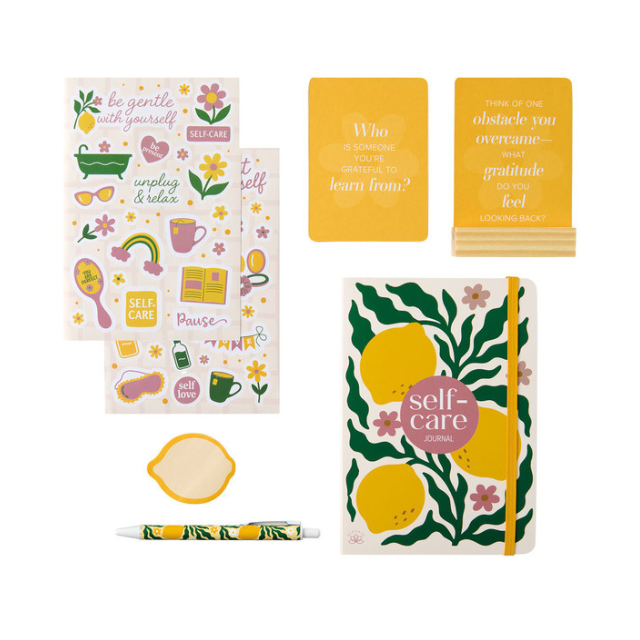 A stationery set including a journal labeled selfcare stickers a lemonshaped dish a pen and two motivational cards