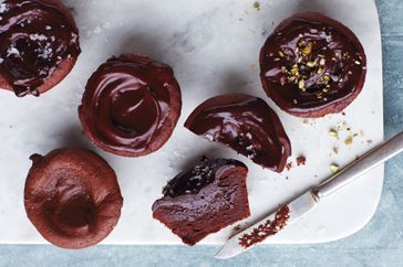 Collection of molten chocolate cupcakes on a cutting board some topped with frosting and garnishes one is cut open to reveal the inside
