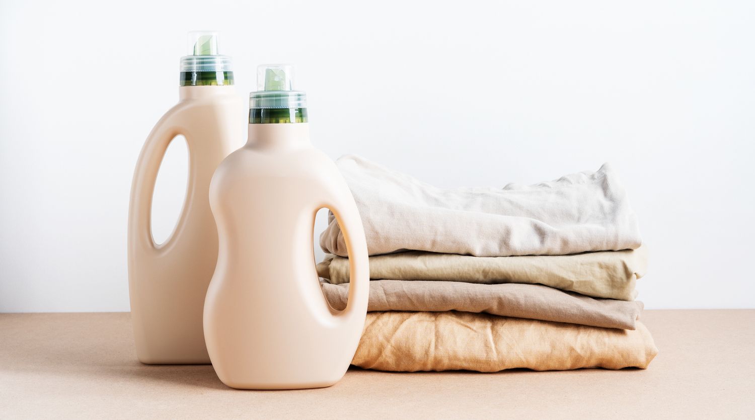 Two detergent bottles placed next to a stack of folded beige textiles on a flat surface