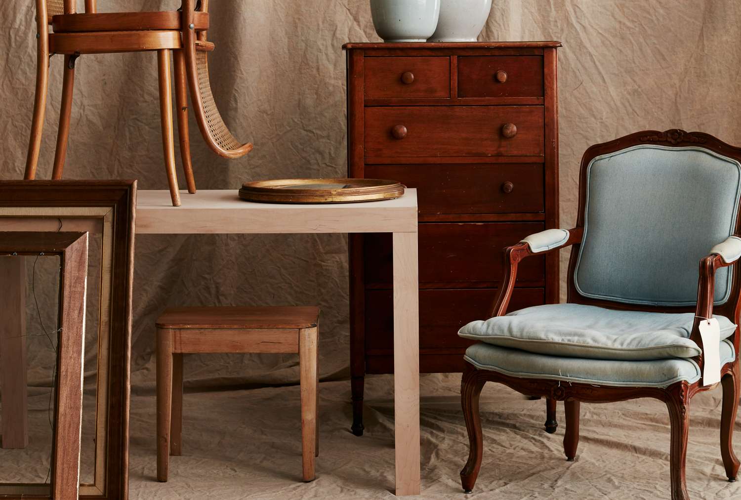 A grouping of wooden furniture pieces including chairs a stool a table and a chest of drawers