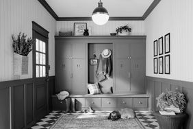 A mudroom with builtin storage cabinets coat hooks a bench and decorative touches such as plants and framed artwork
