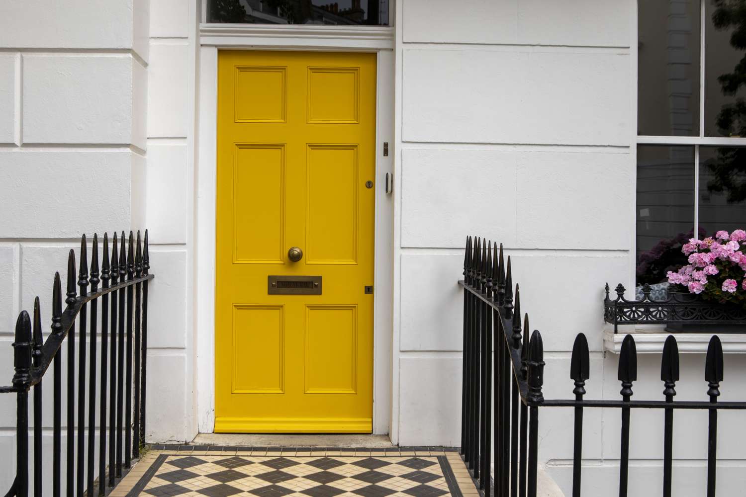 A residential entrance with a patterned tile walkway and a distinctive yellow door flanked by black railing