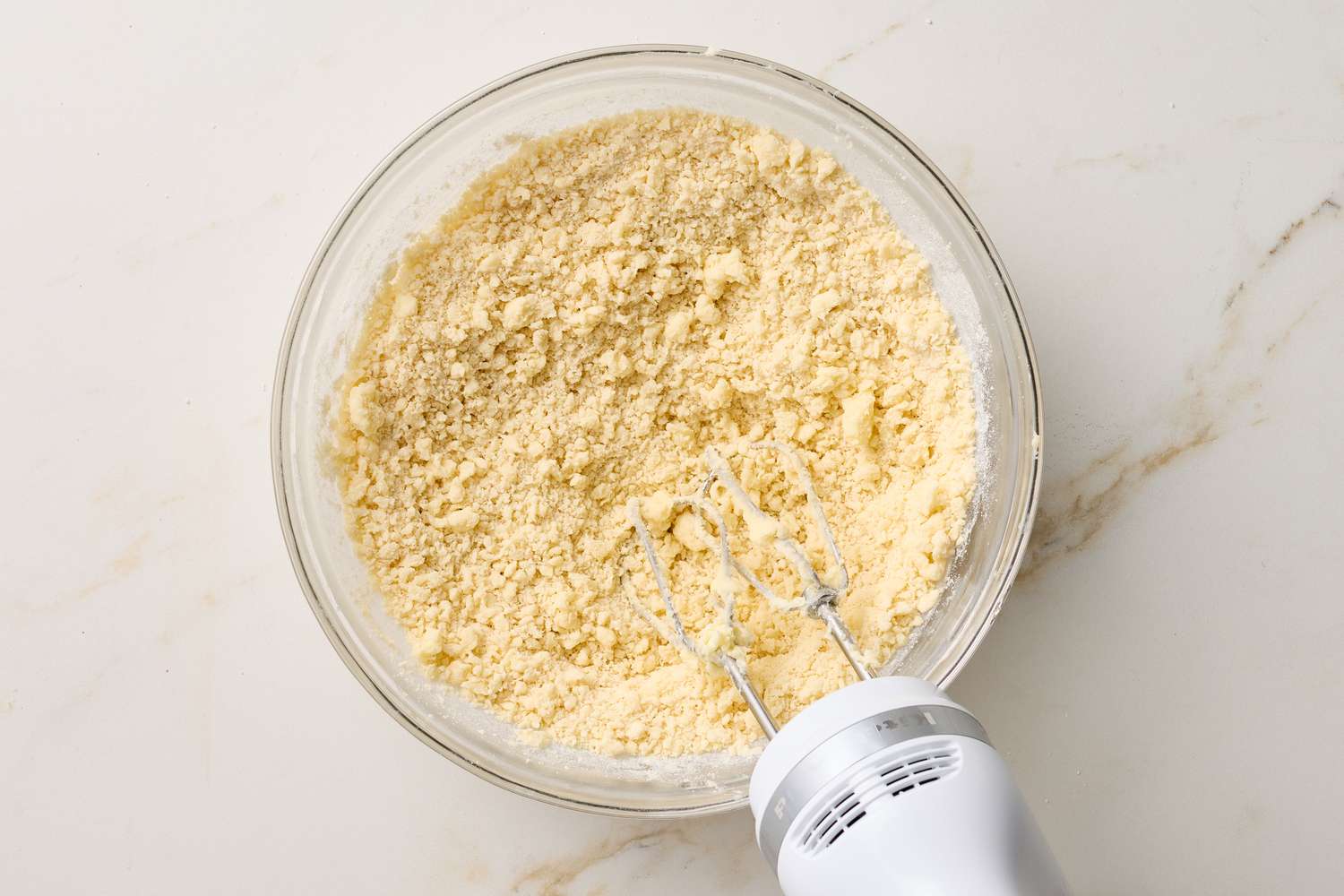 A glass bowl containing shortbread cookie dough mixture with a handheld electric mixer inserted