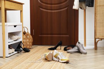 Entryway with scattered shoes a shoe rack and a basket near a door