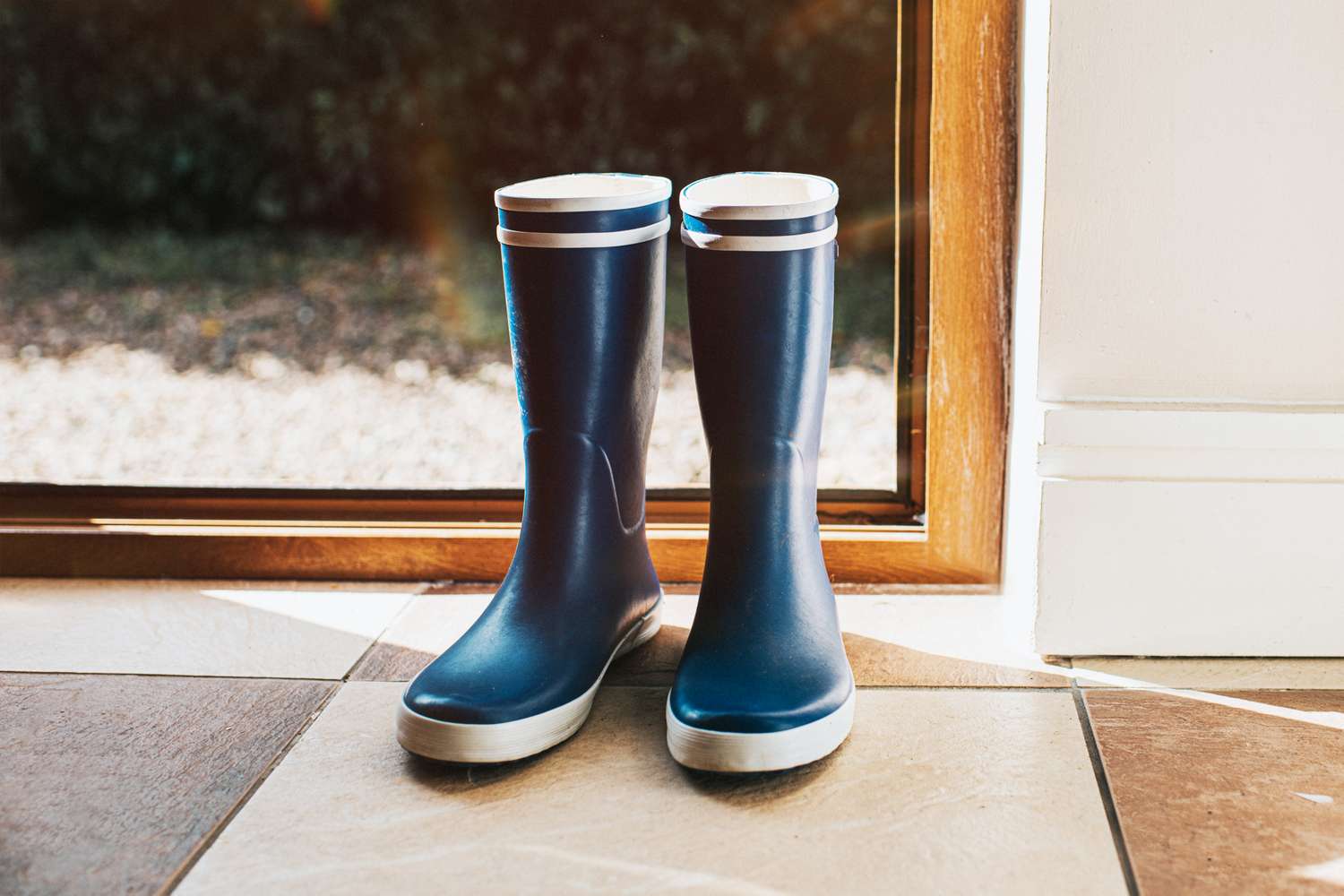 A pair of rain boots placed by a window indoors