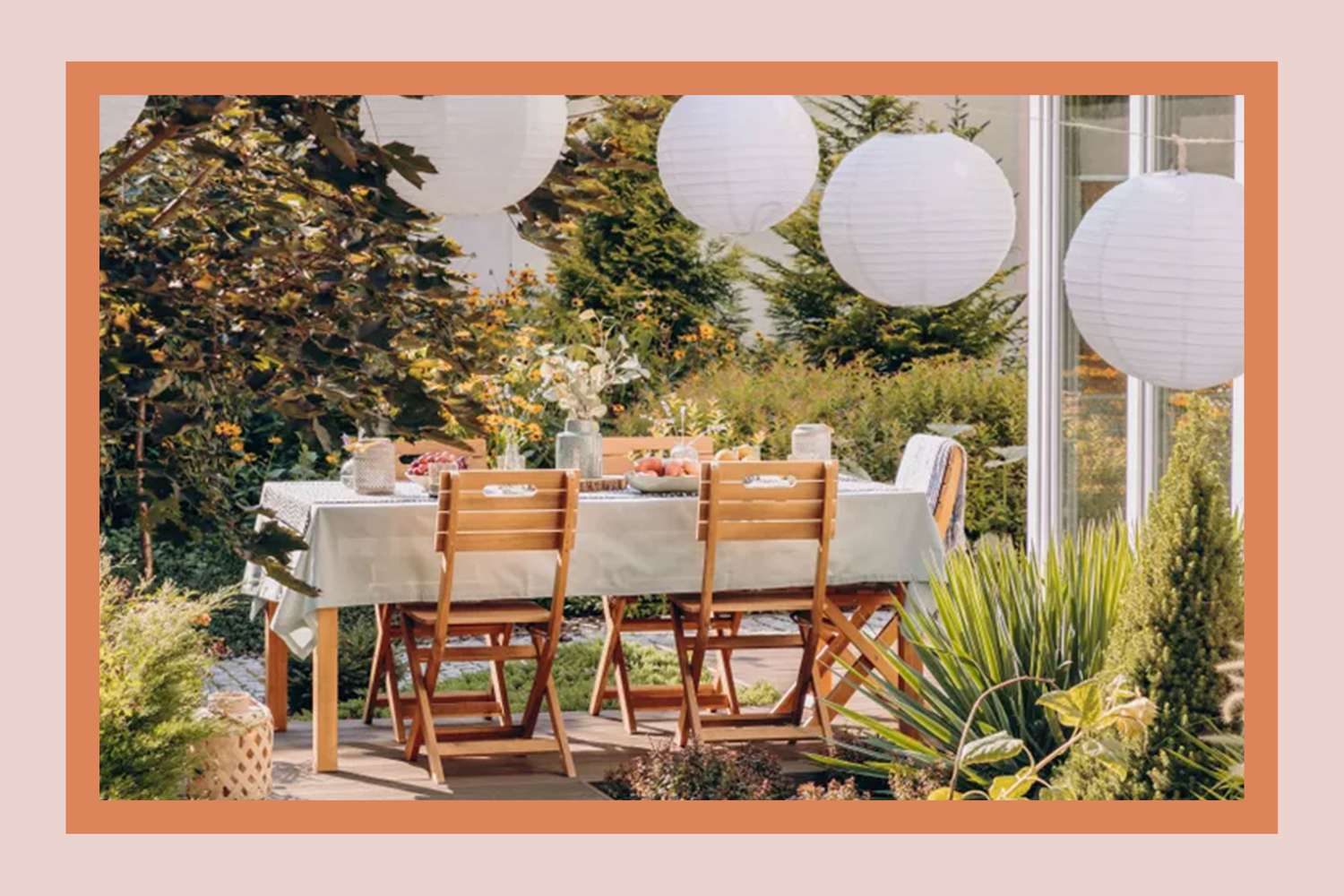 A decorated outdoor dining area with chairs and table set, surrounded by plants and hanging lanterns, in a garden setting