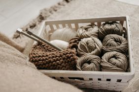 A basket containing balls of yarn knitting needles and a partially knitted piece