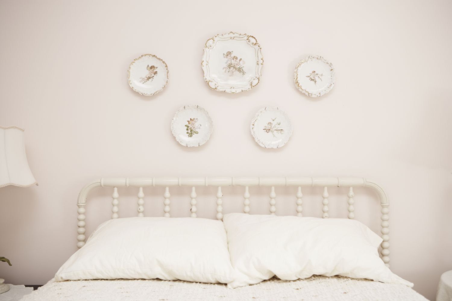 A white bed with pillows beneath decorative plates hung on the wall above it