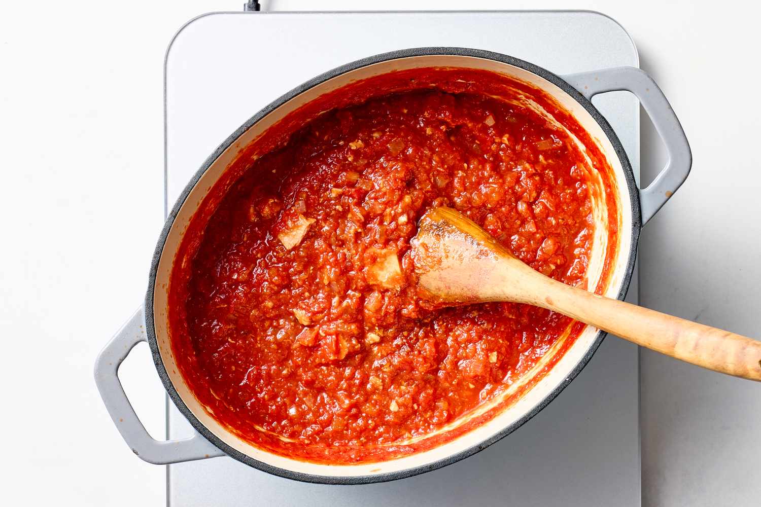 A saucepan filled with tomato paste and a wooden spoon resting inside placed on a stovetoplike surface