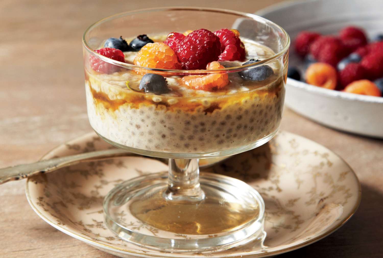 A glass serving bowl of chia pudding topped with assorted berries on a decorative plate