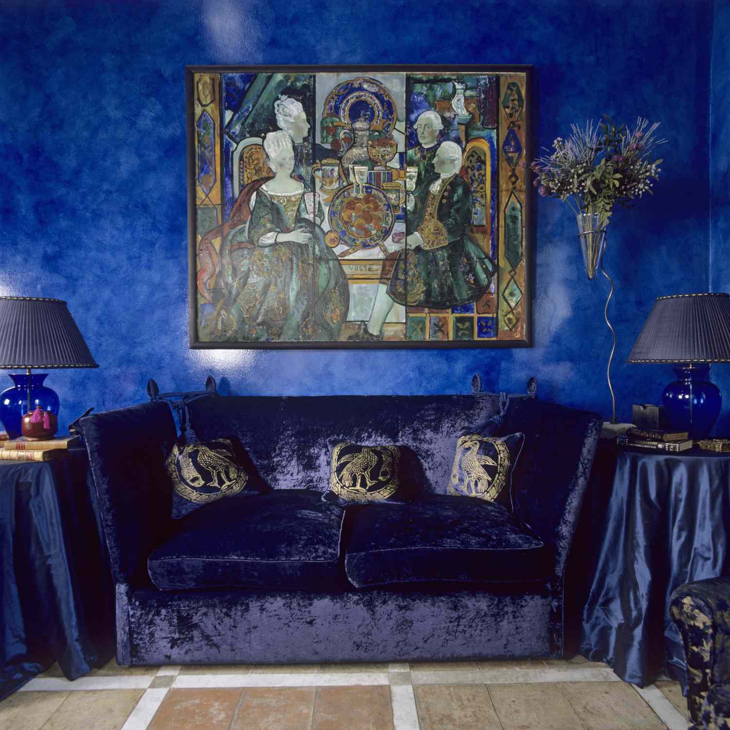 Sofa set with a colorful painting above it surrounded by lamps and decorated side tables