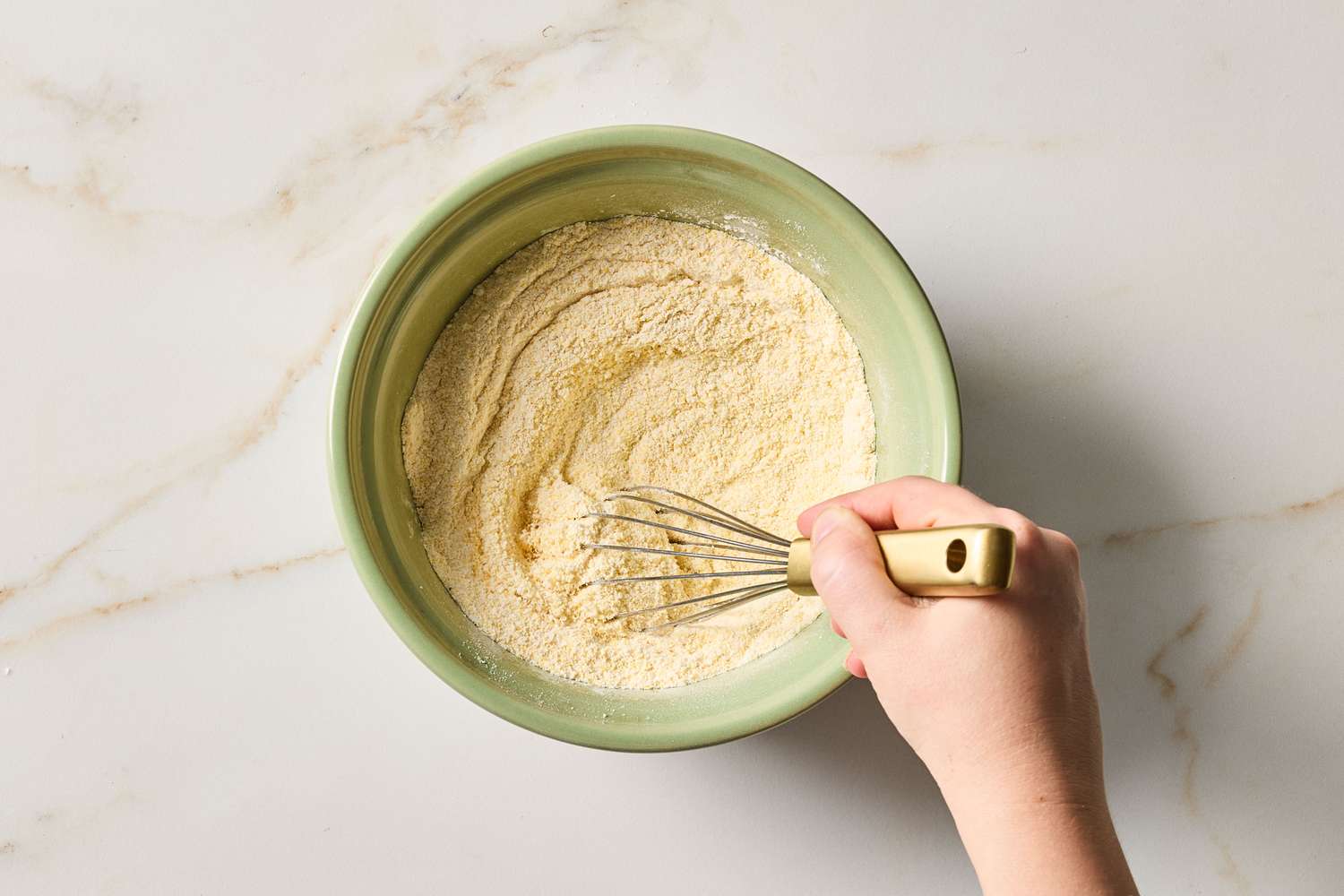 A person whisking dry cornbread mix in a green bowl