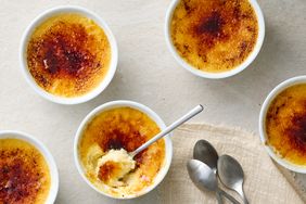 Multiple creme brulee servings in ramekins one partially eaten with spoons beside them on a cloth napkin