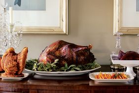 A Thanksgiving dinner setting featuring a turkey on a serving platter surrounded by side dishes on a wooden table