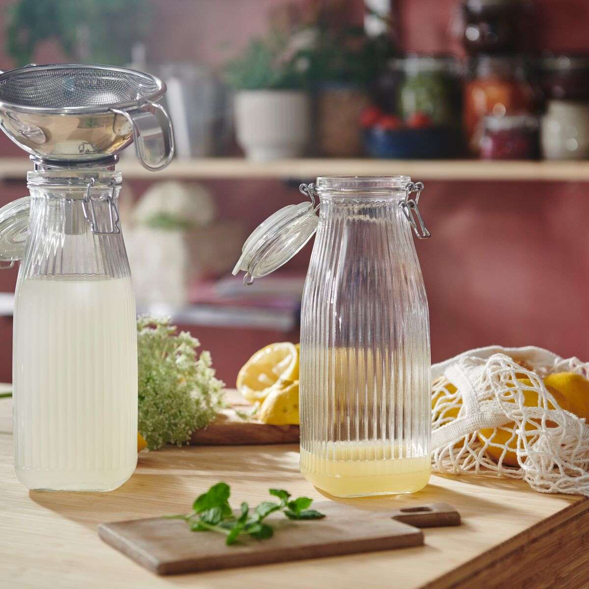 Two glass jars with liquid on a kitchen counter surrounded by lemons and herbs