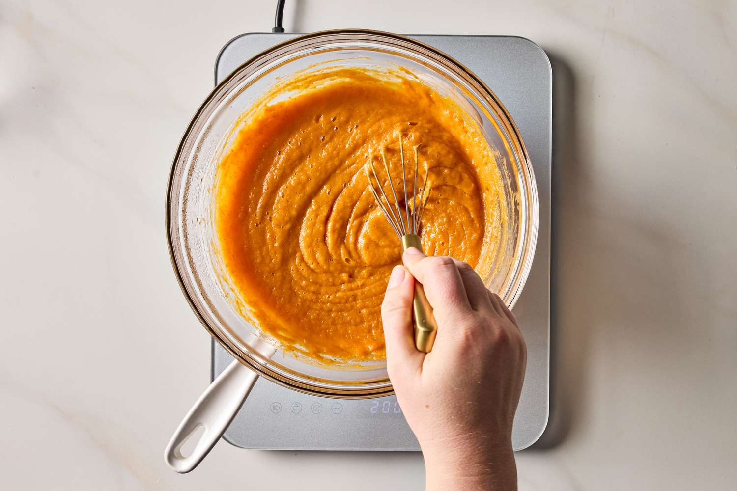 A hand whisking a pumpkin mixture in a clear bowl on a countertop